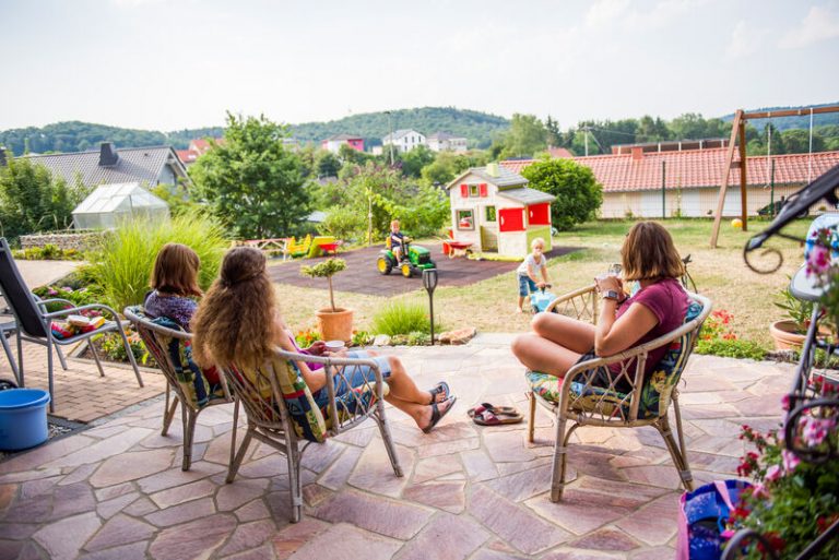 Frauen beim Kaffe auf Tereasse_Kinder im Garten_Häuser im Hintergrund
